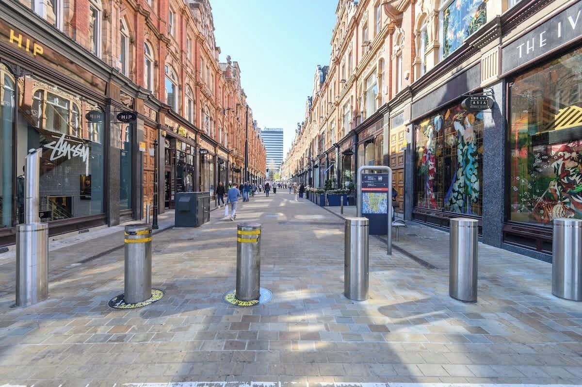 A street with shops on either side, bollards in the middle, and a clear sky.