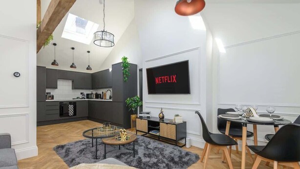 A modern living room with a dining area, a kitchen in the background, and a large TV screen displaying "NETFLIX".