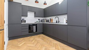 Een moderne keuken met grijze kastjes, een visgraat parketvloer en hanglampen.