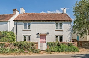 A two-story white house with a red-tiled roof, a pink door, and a white picket fence. - Charming West Wittering Cottage – Cosy Village Retreat, Pet Friendly (West Wittering)