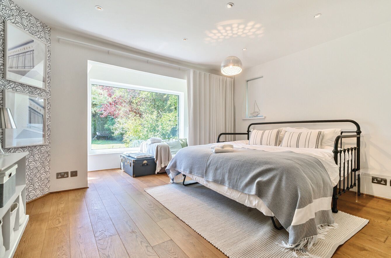 A bedroom with a bed, a window with a view of greenery, a dresser, and a mirror.