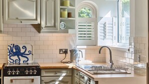 A kitchen with white cabinets, a stove, and a window with blinds. - Stylish West Wittering Retreat Near Beach – Thessaly, Sleeps 8, Pet Friendly (West Wittering)