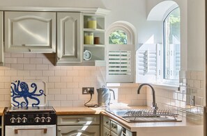 Una cocina con gabinetes blancos, una estufa y una ventana con persianas.
