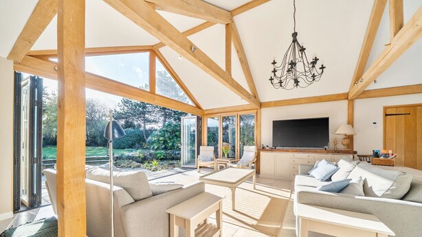 A spacious living area with a large TV, wooden beams, and a view of the outdoors. - West Wittering Family Beach Escape – Sleeps 8, Garden & Dog Friendly (West Wittering)