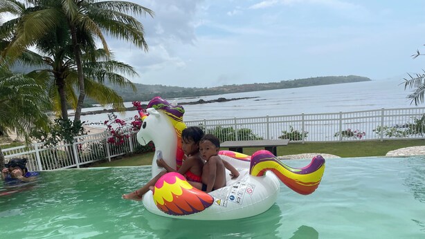 Ein Pool mit aufblasbaren Einhorn-Schwimmfiguren, Palmen und Blick aufs Meer.