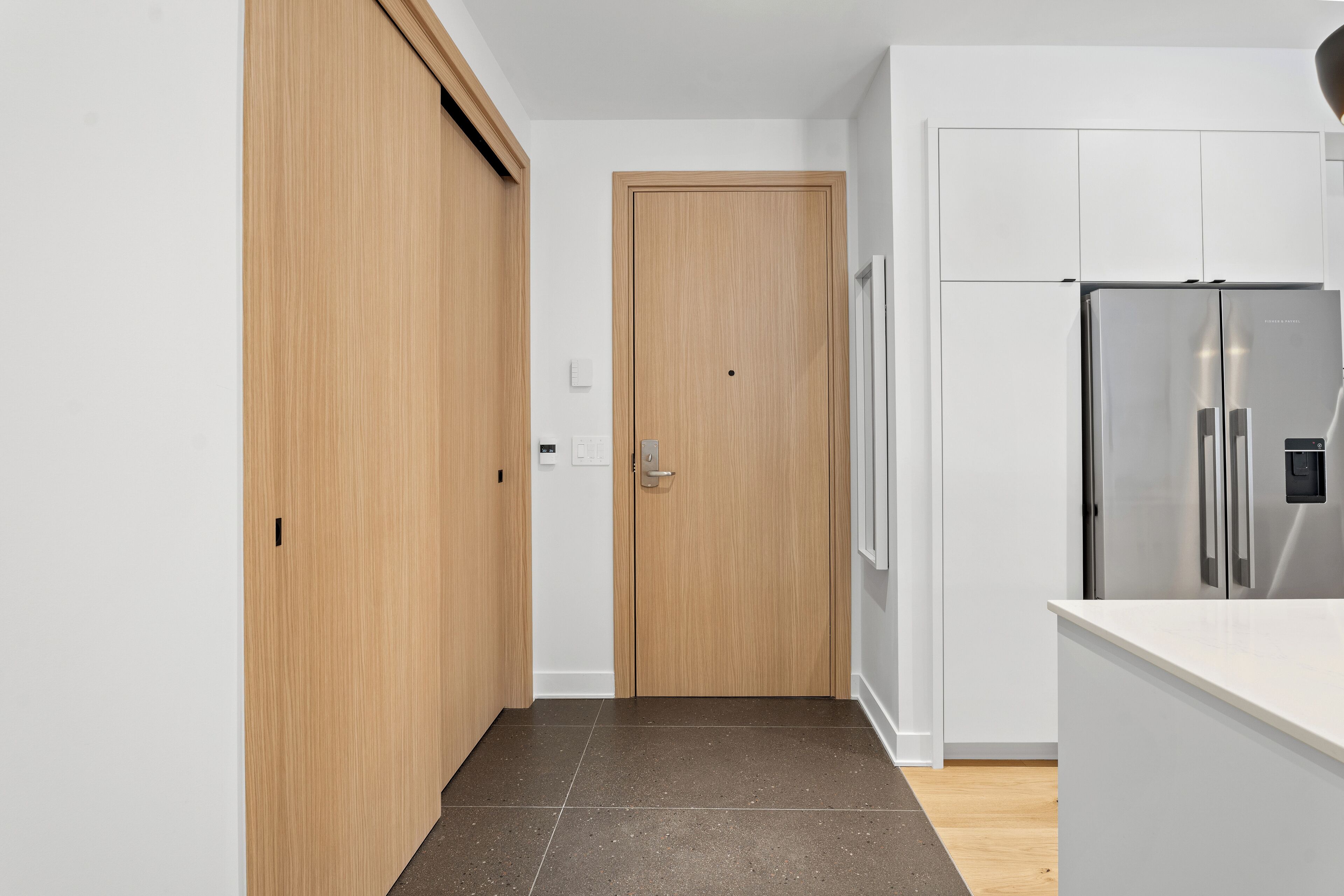 Une cuisine moderne dotée d’un réfrigérateur en acier inoxydable, de meubles en bois et d’un plan de travail blanc.