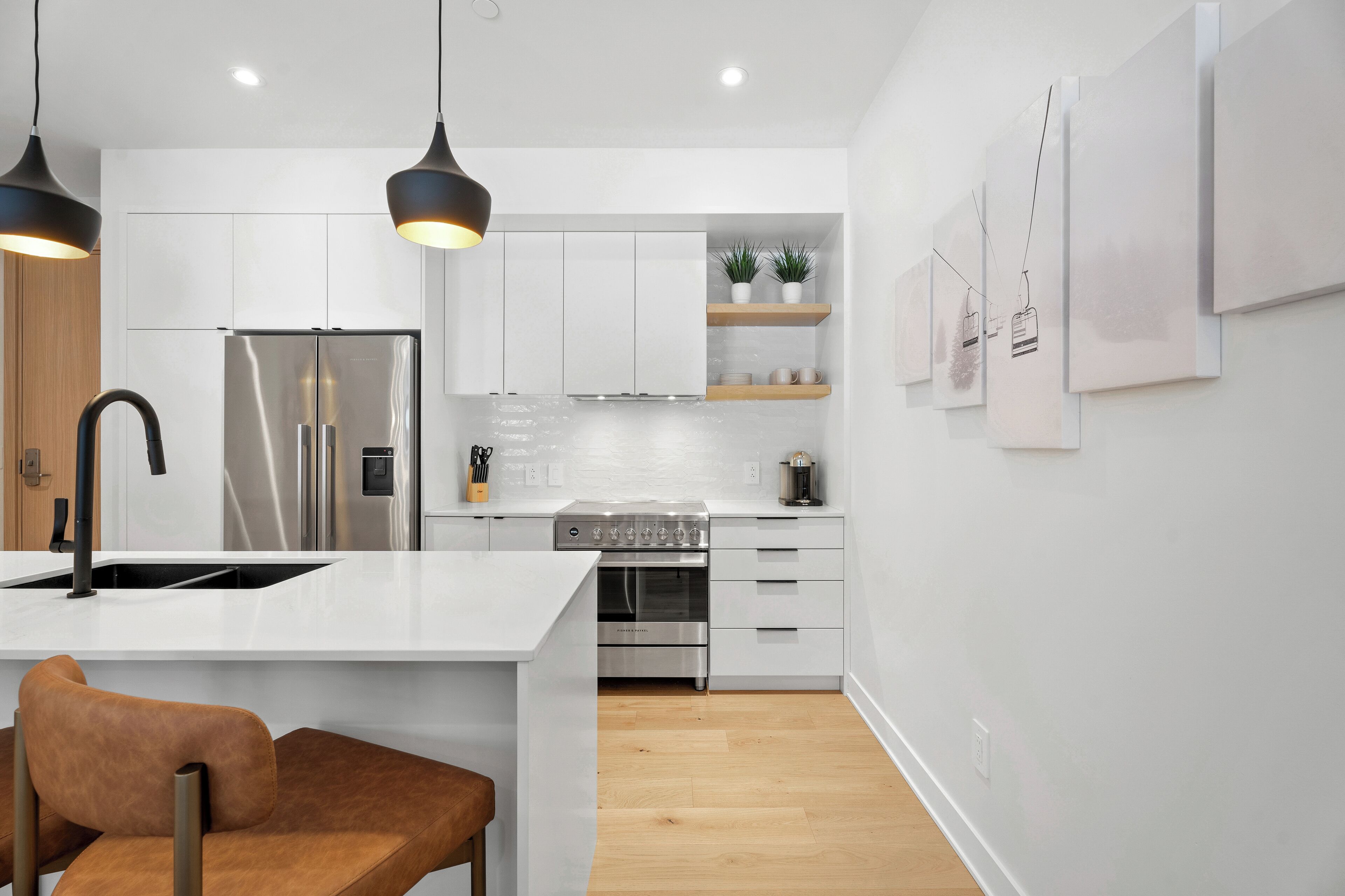 Una cocina moderna con armarios blancos, electrodomésticos de acero inoxidable e iluminación colgante.