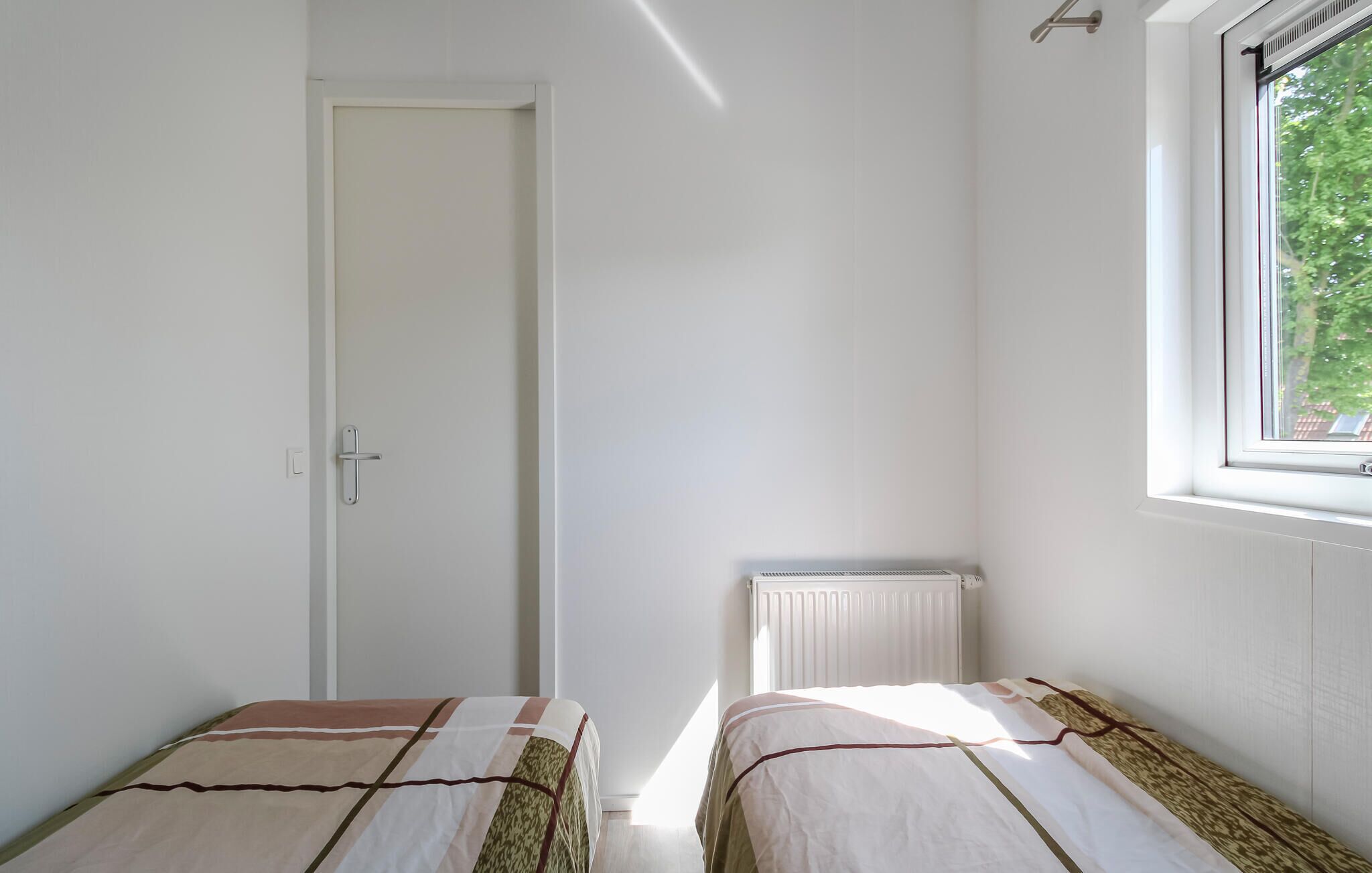 A small, clean room with two beds, a radiator, a window with a view of trees, and a door.