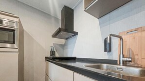 A modern kitchen with a stainless steel sink, a built-in oven, and a black range hood. - 2 bedroom cozy home in Den Oever (Den Oever)
