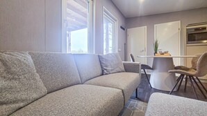 A modern living room with a grey sofa, a dining table with chairs, and a kitchen area in the background. - 2 bedroom cozy home in Den Oever (Den Oever)