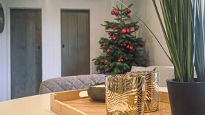 A wooden tray with a candle and two patterned glass containers on a table. A potted plant and a Christmas tree with red ornaments are in the background. - 2 bedroom cozy home in Den Oever (Den Oever)