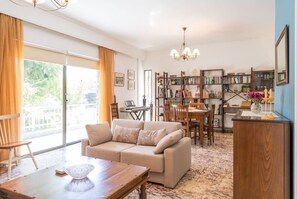 Ein geräumiges Wohnzimmer mit einer Couch, einem Esstisch und einer Kristallleuchter. Ein Bücherregal ist mit Büchern und Dekoration gefüllt.