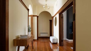 A hallway with wooden flooring, a white bench, a small table with a plant, and a round mirror on the wall. - Charm & Modern Comfort in East Launceston (East Launceston)
