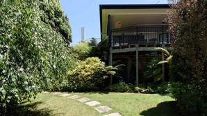 A modern building with a balcony, surrounded by lush greenery and a stone pathway. - Charm & Modern Comfort in East Launceston (East Launceston)