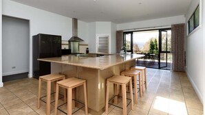 A modern kitchen with a central island, bar stools, a built-in stove, and a large window overlooking a garden. - Charm & Modern Comfort in East Launceston (East Launceston)