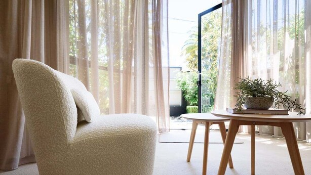 A room with a plush white armchair, a round wooden table with a potted plant, and sheer curtains allowing natural light. - Charm & Modern Comfort in East Launceston (East Launceston)
