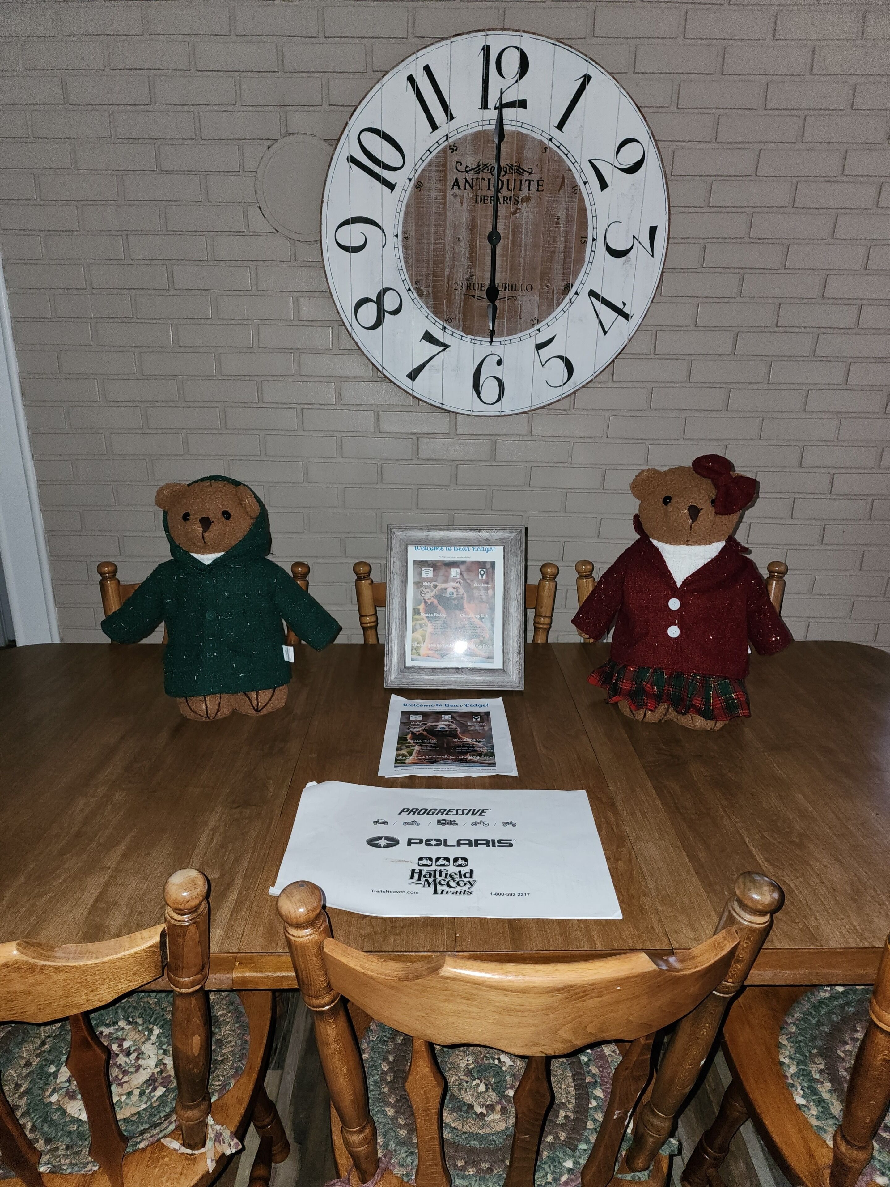 Une table à manger en bois, ornée de deux ours en peluche, d’une pancarte d’accueil encadrée et d’un menu.