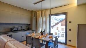 Een moderne keuken met een eethoek, een bank en uitzicht op bergen door een groot raam.