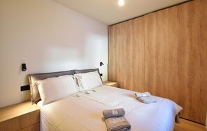 A neatly made bed with white linens and a folded towel, a wooden nightstand with a lamp, and a wooden wardrobe against the wall. - Residenza panoramica 2 (Ponte di Legno)