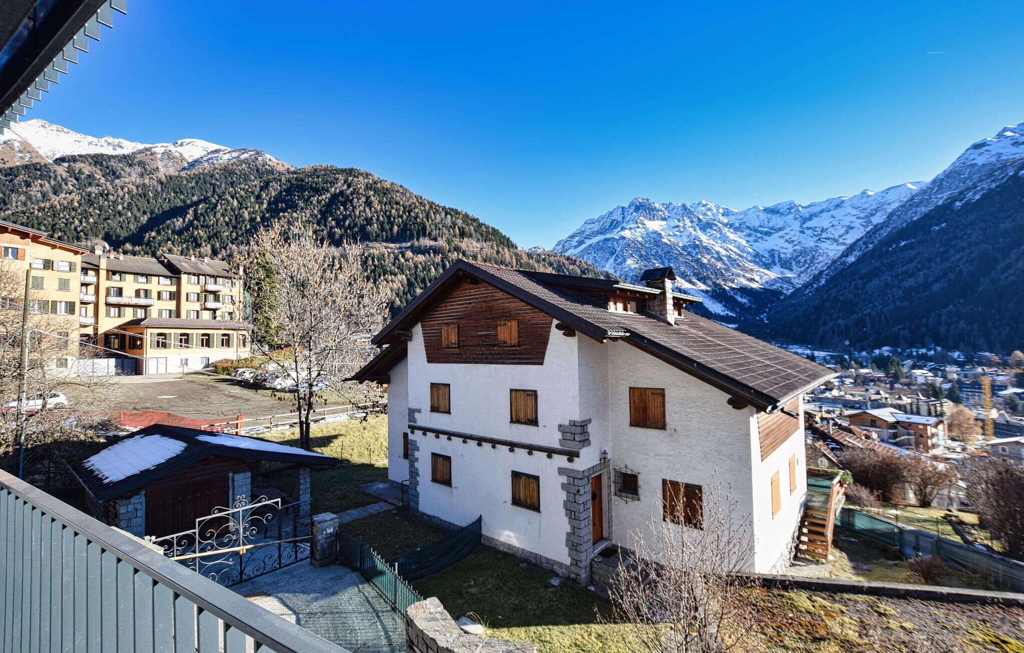 Un bâtiment de style chalet traditionnel, doté d’une façade en pierre et de détails en bois, entouré d’un paysage montagneux et d’un petit village.