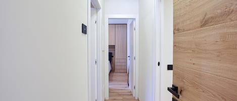 Un pasillo estrecho con suelo de madera, paredes blancas y una puerta de madera a la derecha.