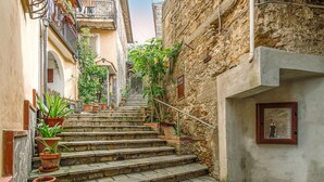 Una estrecha escalera de piedra en un edificio histórico, con macetas en los escalones y un pequeño balcón con barandilla.