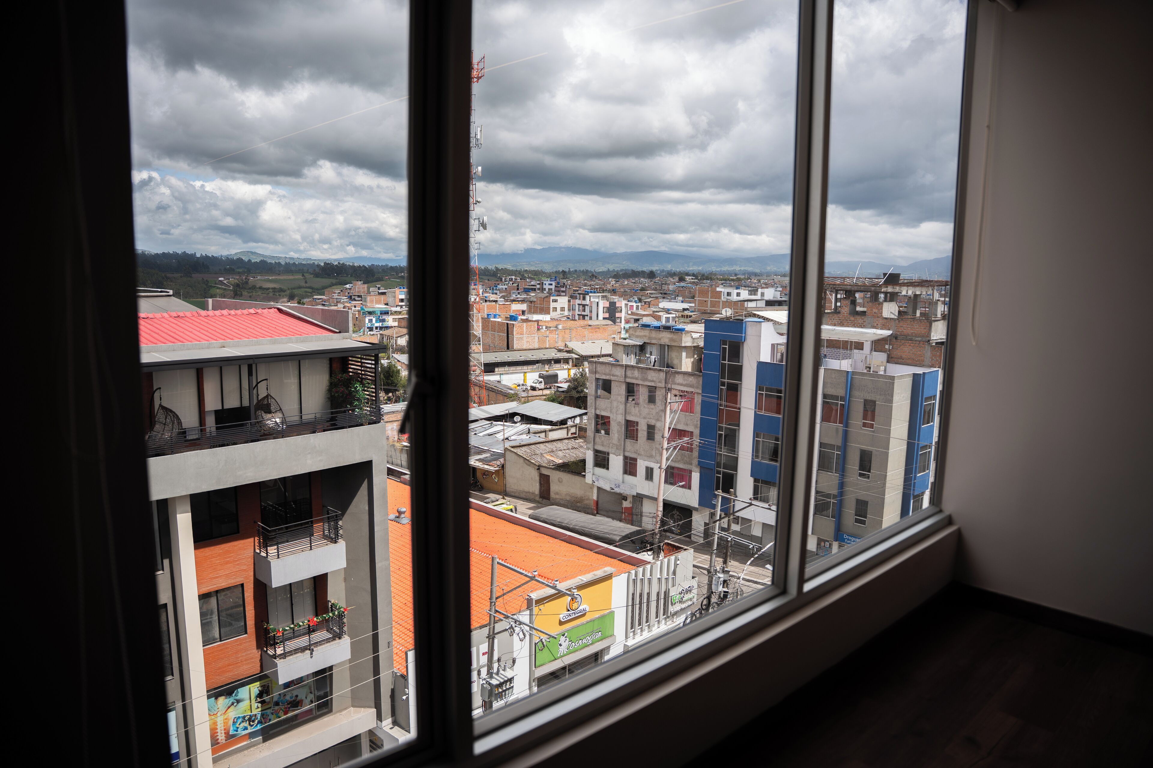 Vista desde una ventana sobre un paisaje urbano con edificios y cielo nublado.