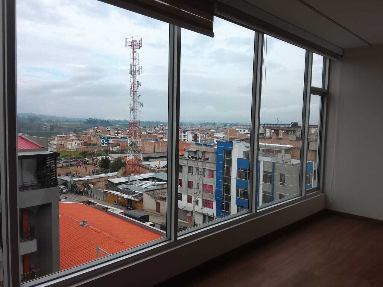 Una habitación con ventanas amplias que ofrecen vistas de un paisaje urbano con edificios y una torre de comunicaciones.