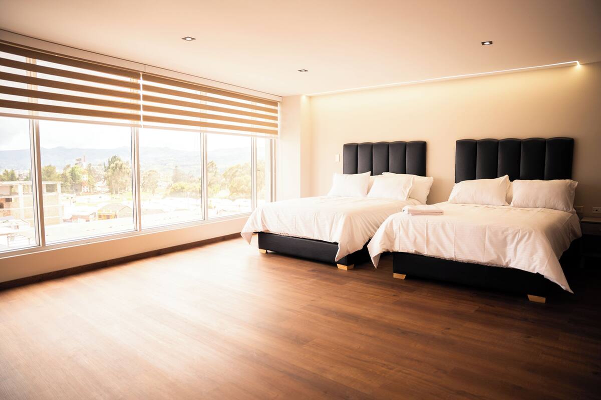 Habitación de hotel moderna con dos camas, ventanas amplias y vista a la ciudad.