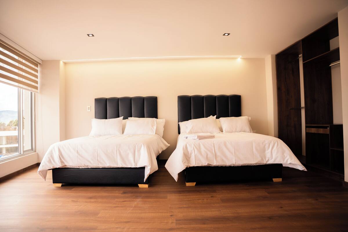 Un dormitorio moderno con dos camas, suelo de madera y un ventanal grande.