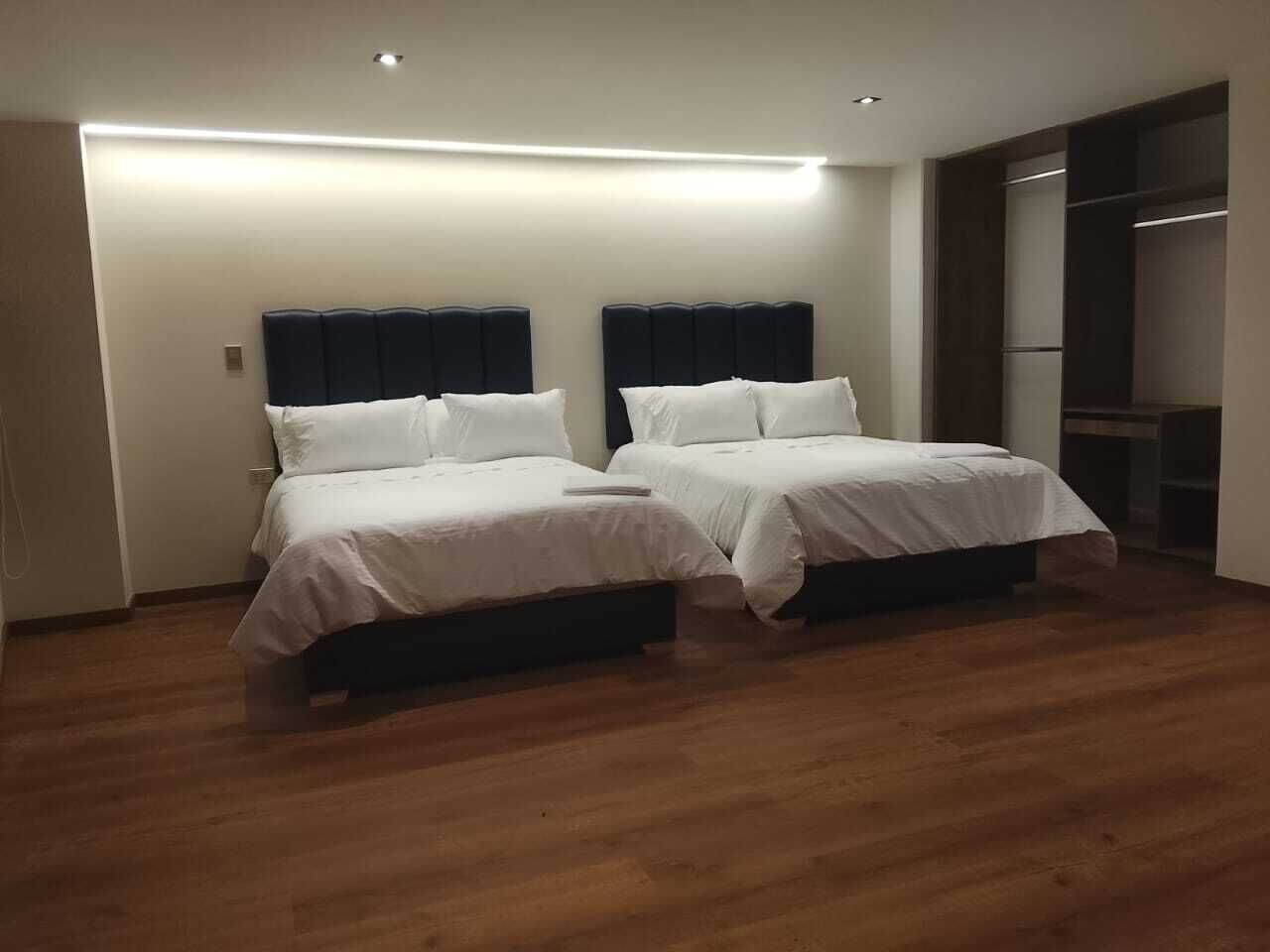 A hotel room with two beds, wooden flooring, and a built-in wardrobe.