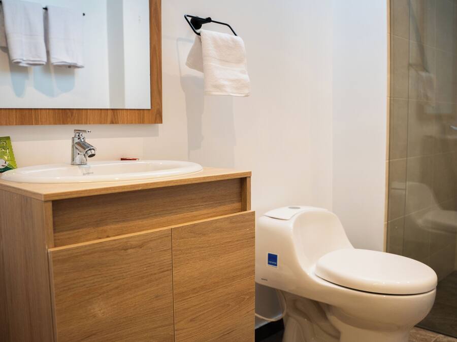 Moderni kylpyhuone, jossa on puinen allaskaappi, valkoinen pesuallas, wc ja lasinen suihkuseinä.