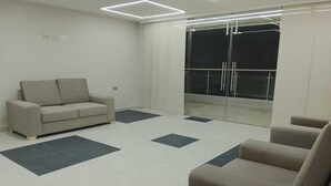Une pièce moderne et minimaliste, avec un canapé, un fauteuil et une porte vitrée donnant sur un balcon.