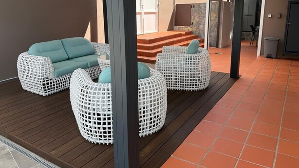 Een overdekt terras met rieten meubels en een stenen muur op de achtergrond.