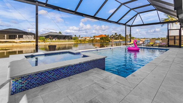 An indoor swimming pool with a glass ceiling, a floating pink flamingo, and a view of surrounding buildings. - Luxury Coastal Living with Water Views, Pool & Spa (Cape Coral)