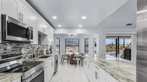 A modern kitchen with a central island, built-in appliances, and a view of a swimming pool. - Luxury Coastal Living with Water Views, Pool & Spa (Cape Coral)