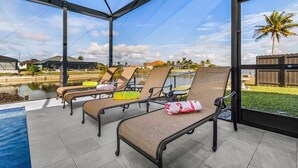 A covered outdoor area with lounge chairs and a pool. - Luxury Coastal Living with Water Views, Pool & Spa (Cape Coral)