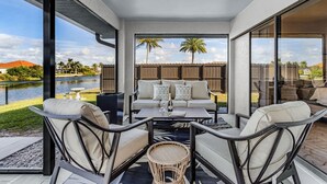 A covered patio area with a sofa set, a table, and chairs. - Luxury Coastal Living with Water Views, Pool & Spa (Cape Coral)