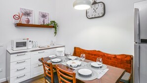 Moderni keittiö, jossa on valkoiset kaapit, mikroaaltouuni ja ruokapöytä neljälle henkilölle.