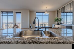 A kitchen with a granite countertop, stainless steel sink, and a dining area with a table and chairs. - Luxurious Downtown High floor Corner-2bd2bth-#420- Parking included (Nashville)