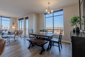 A dining area with a wooden table and benches, large windows with a city view, a chandelier, and a plant on a console table. - Luxurious Downtown High floor Corner-2bd2bth-#420- Parking included (Nashville)