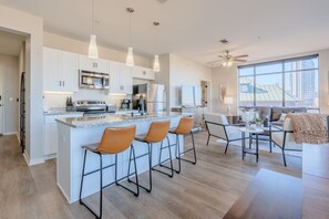 A modern kitchen with white cabinets, a central island with bar stools, a ceiling fan, and a large window offering a city view. - Luxurious Downtown High floor Corner-2bd2bth-#420- Parking included (Nashville)