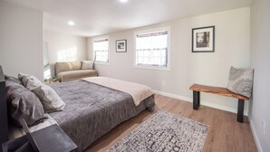 Quarto com cama, um banquinho, tapete e quadros nas paredes.