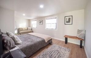 A bedroom with a bed, a bench, a rug, and framed pictures on the wall. - Grover Beach Getaway near beach, downtown & dunes! (Grover Beach)