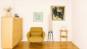 A room with a wooden wardrobe, a mustard-colored armchair, a small table with a vase, and two framed artworks on the wall. - GBH - Central Skagen Townhouse (Skagen)