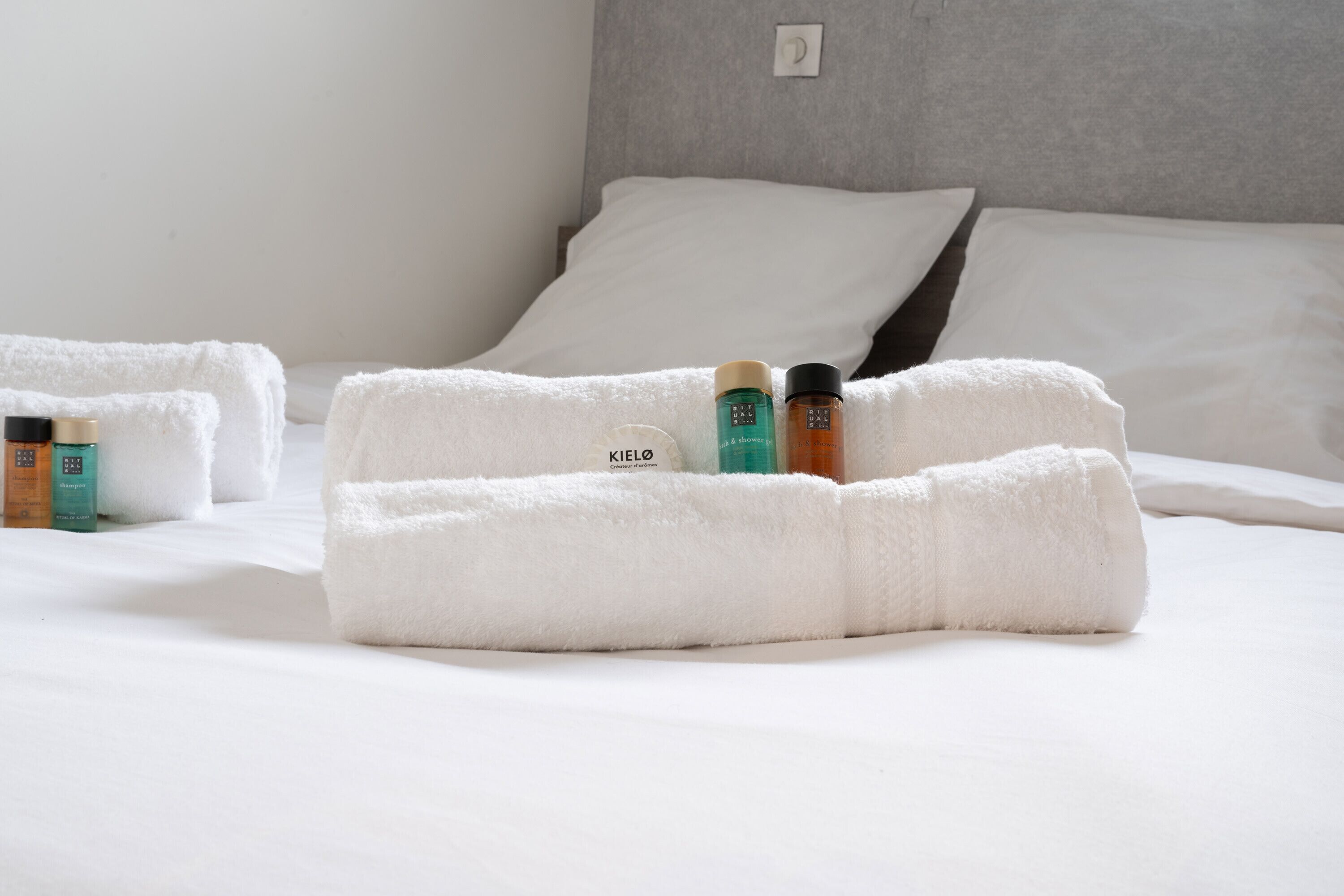 A neatly made bed with white linens, a grey headboard, and a set of toiletries on the bed.