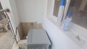 A corner of a room with a grey utility box, a window with a screen, and a water bottle on the windowsill.