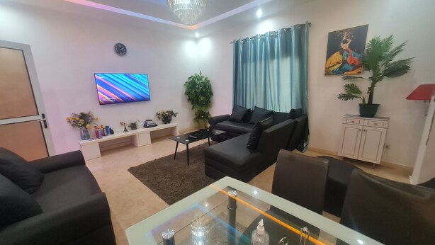 A modern living room with a sofa set, a glass coffee table, a TV, and a chandelier.