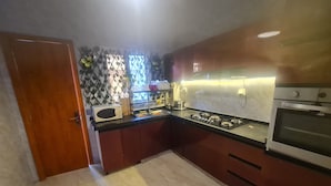 A kitchen with a microwave, stove, and oven. There is a window with a decorative screen and a door on the left.