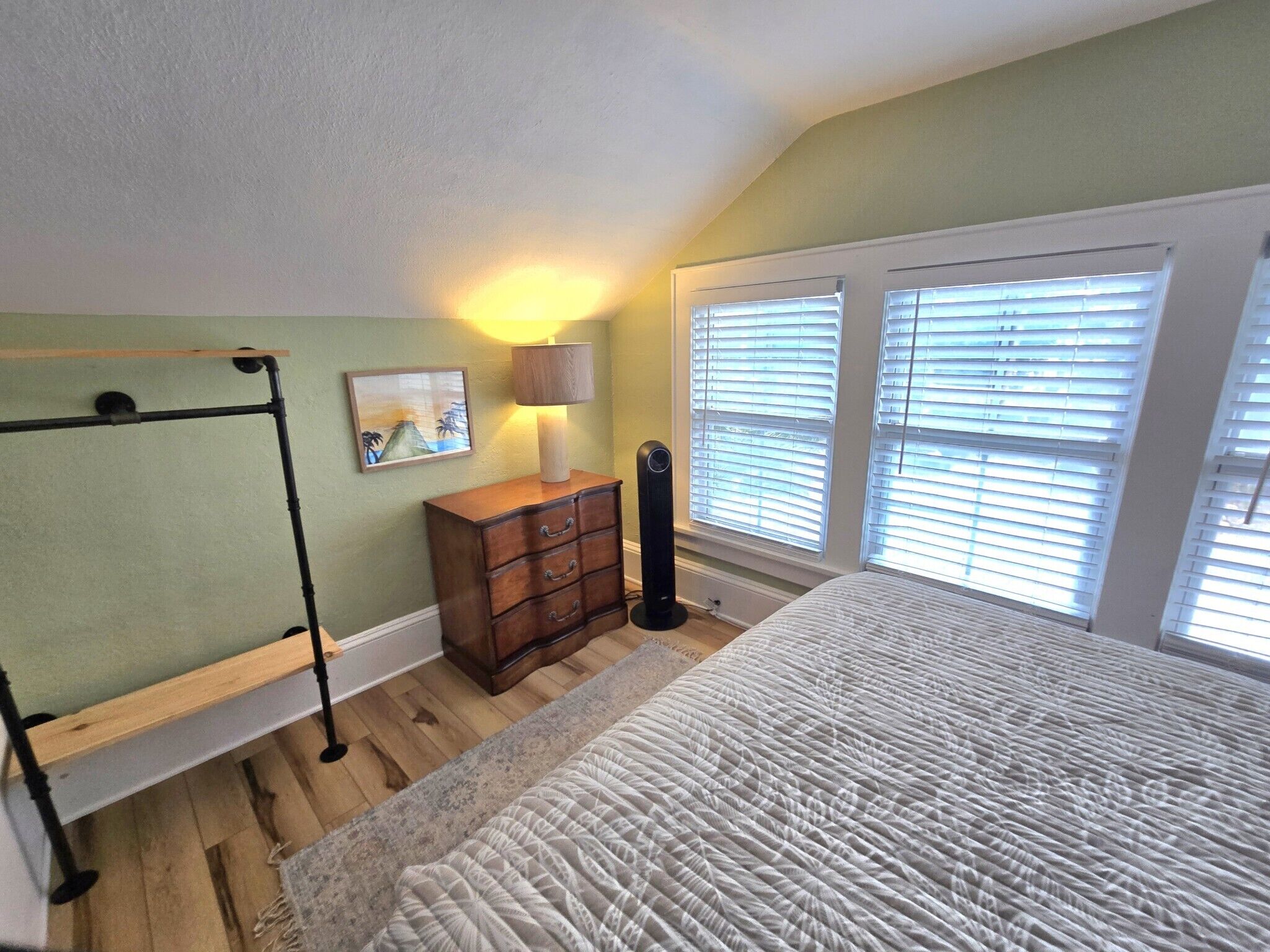Une chambre à coucher avec un lit, une commode, une lampe, un radiateur et une fenêtre avec des stores.